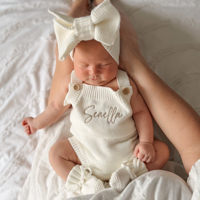 White knit romper with bow straps and front script name, gathered ruffle cuffs
