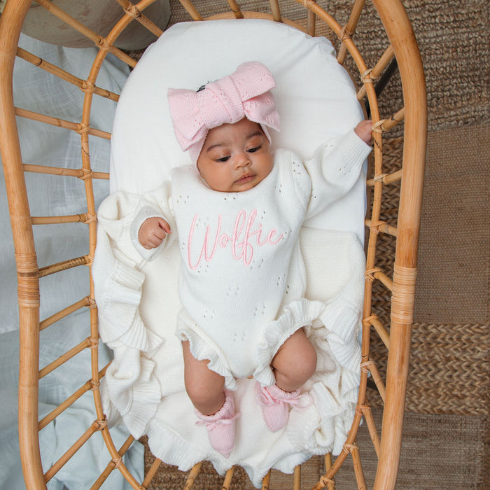 White knit baby romper with pointelle detail, pink bow headband, and ruffled cuffs