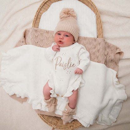 White knitted pointelle romper with long sleeves, ruffled cuffs, and snap buttons