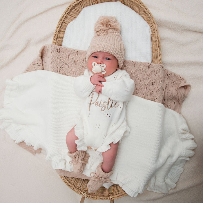 White knitted pointelle romper with long sleeves and ruffled leg openings, beige beanie