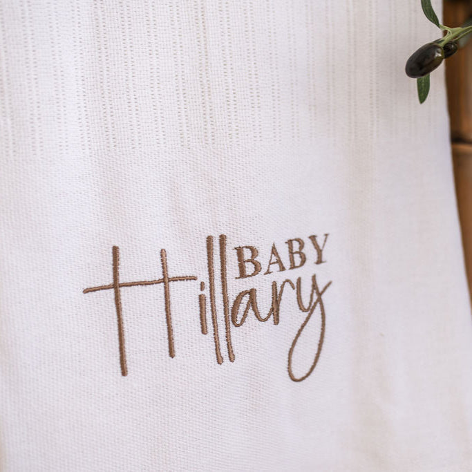 Tight close-up of 'Baby Mary' embroidery on white knitted baby blanket