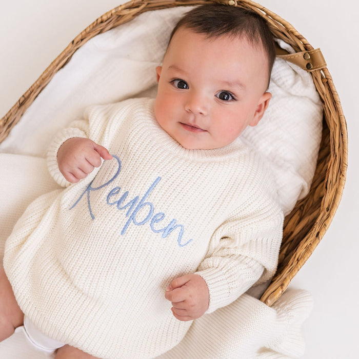 Personalized knitted baby jumper in white with blue 'Reypen' script, close-up