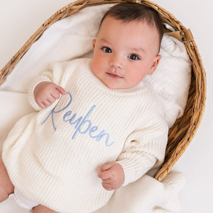 Personalized knitted baby jumper in white with blue 'Reypen' script, close-up
