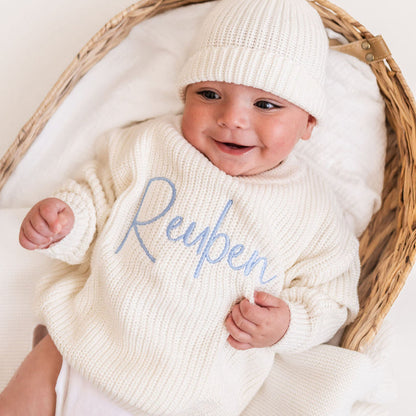 Personalized knitted baby jumper in white with blue 'Reypen' script and knit beanie