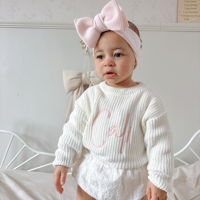 White knitted baby jumper with pink script detail on chest, long sleeves