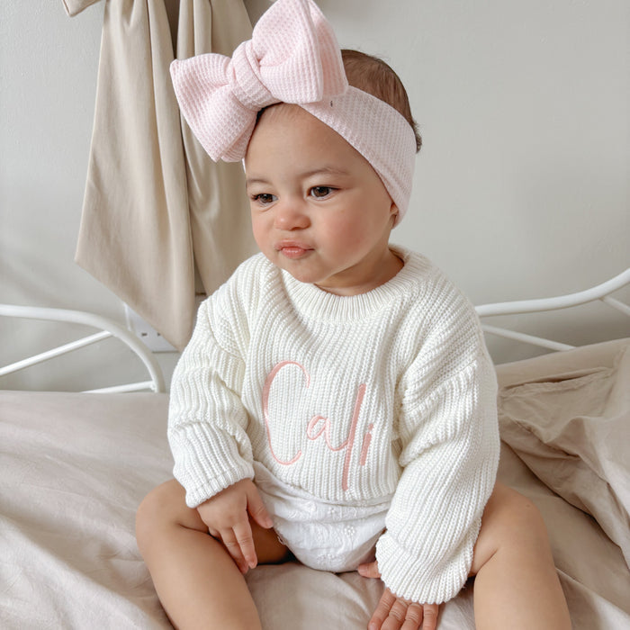 White knitted baby jumper with pink script detail on chest, ribbed crew neck