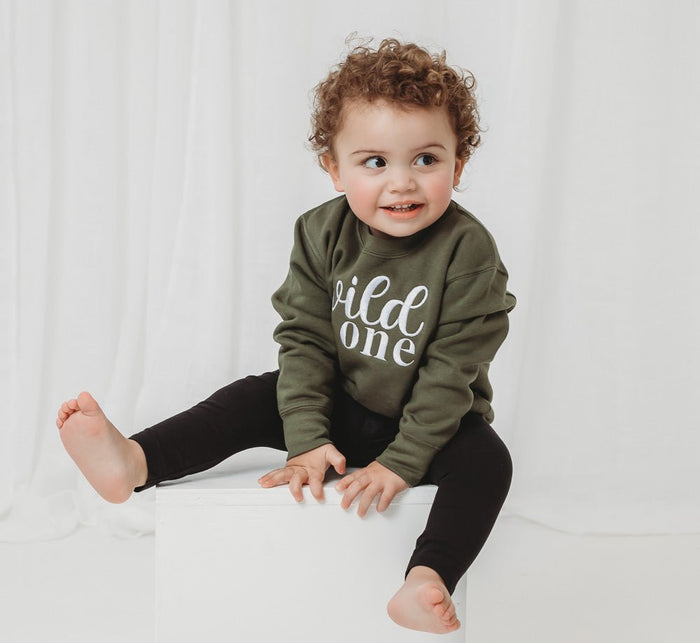 Olive green kids birthday sweater with white “wild one” lettering, long sleeves
