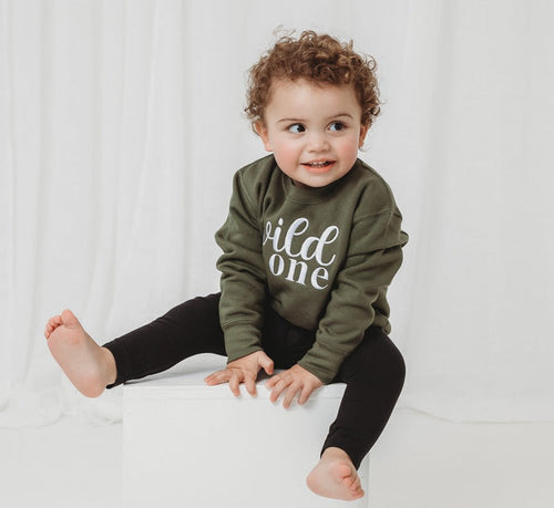 Olive green kids birthday sweater with white “wild one” lettering, long sleeves