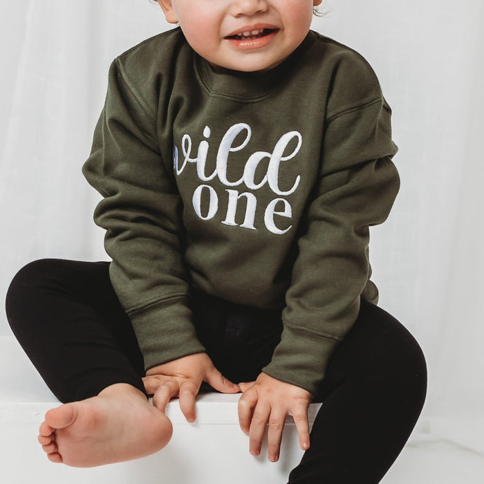 Olive green kids birthday sweater with white “wild one” print on chest, long sleeves