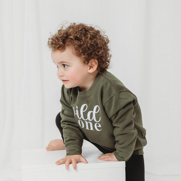 Olive green kids birthday sweater with white “wild one” lettering, side view